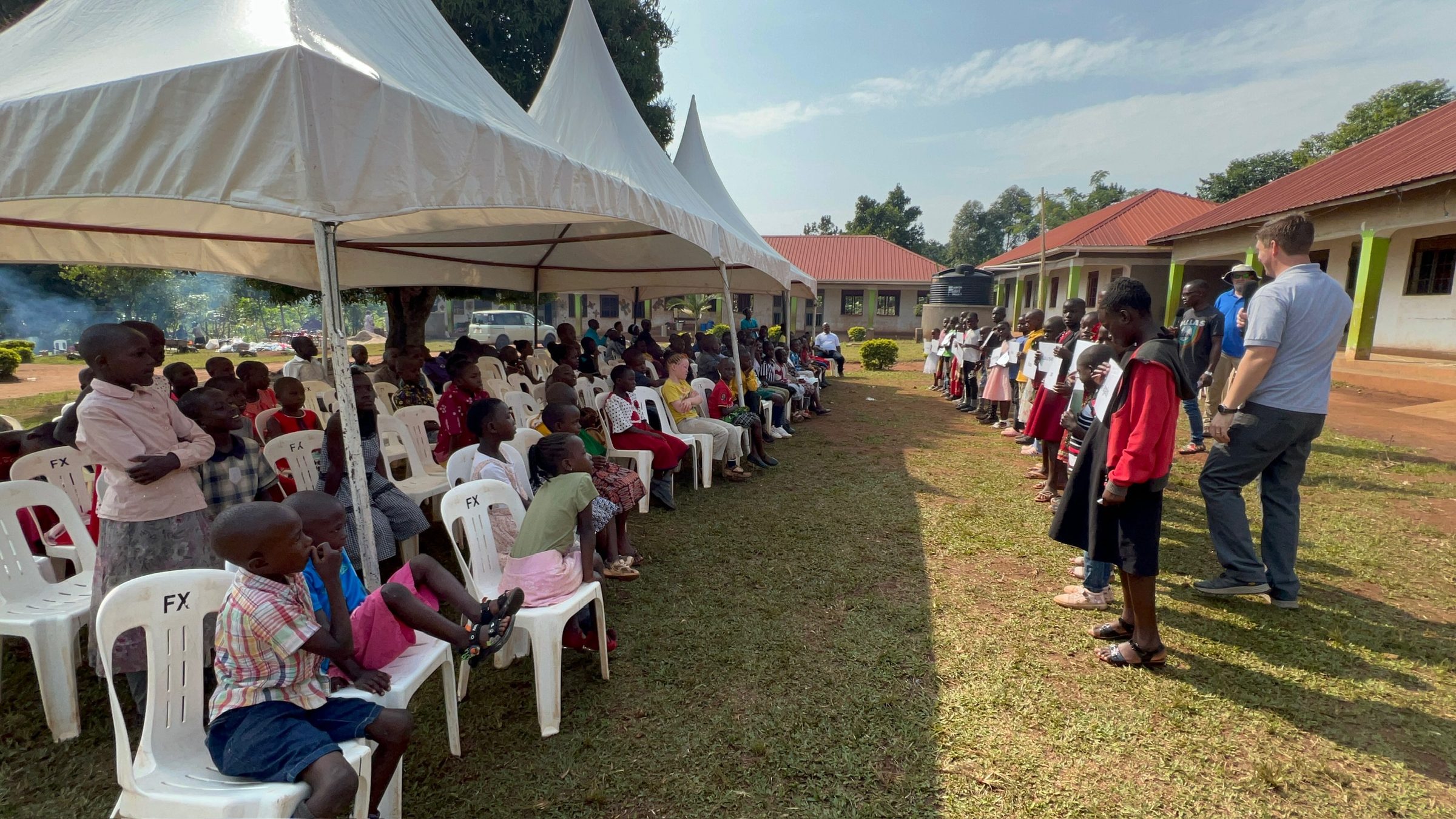 Children seated under tents at a Children's Symposium while a line of children recites memory verses.