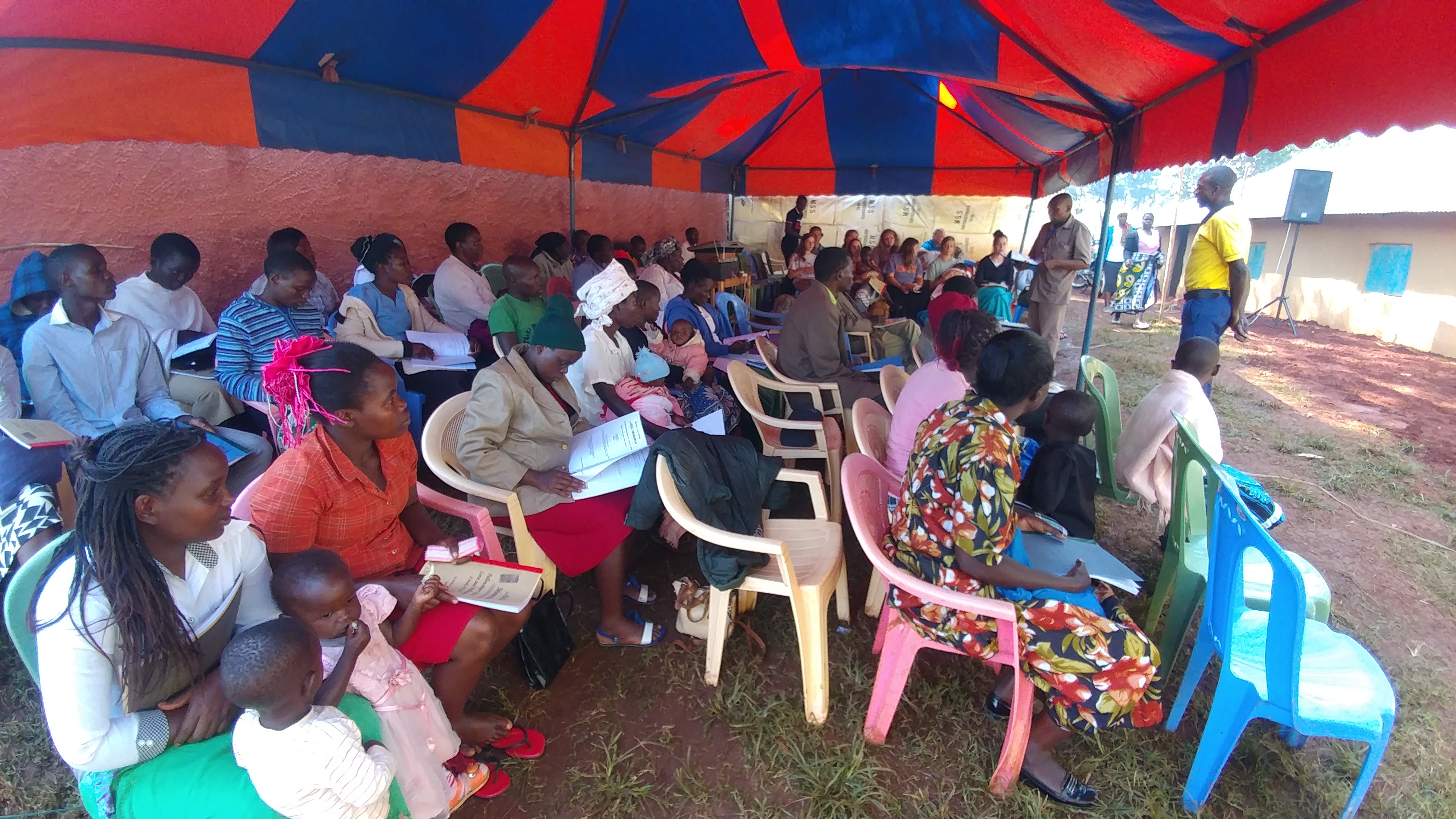 Congregation under a hire tent with workbooks open and a local teacher at the front, 2019.
