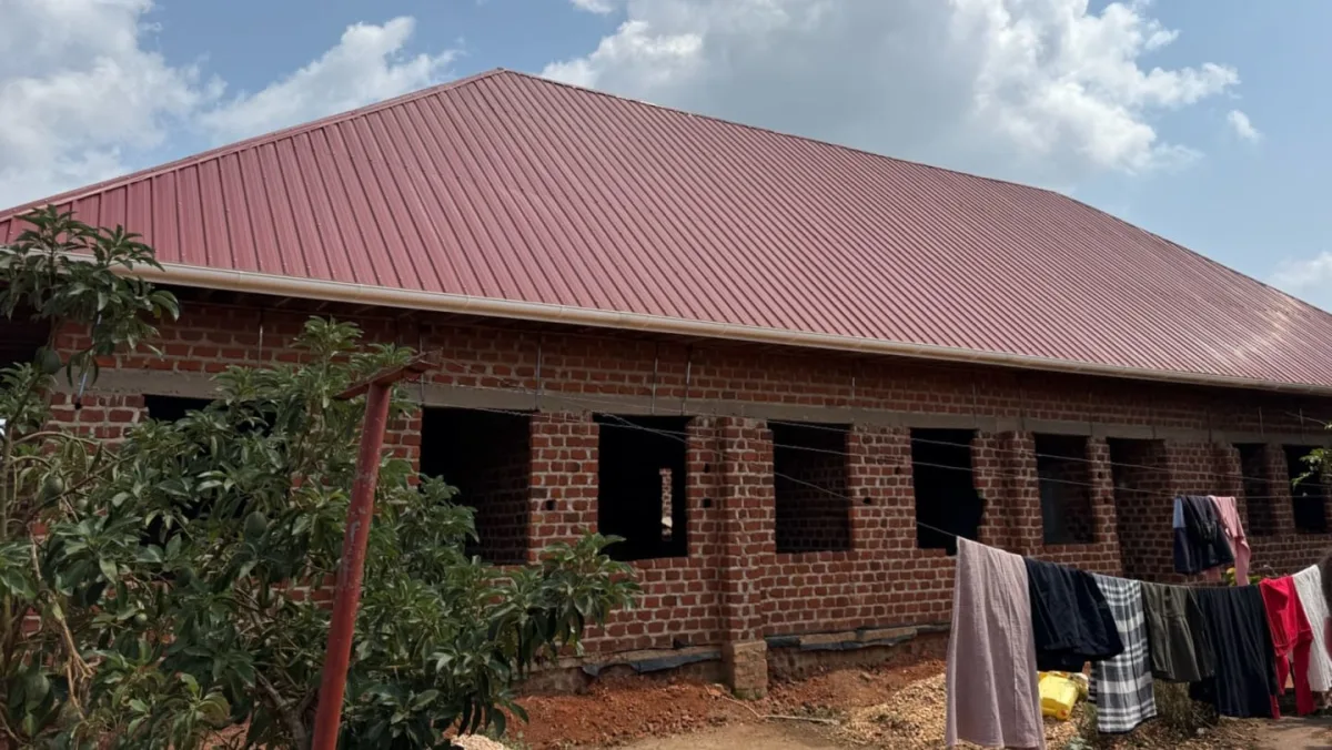 Girls' dormitory with completed red metal roof, empty window openings, 2024.