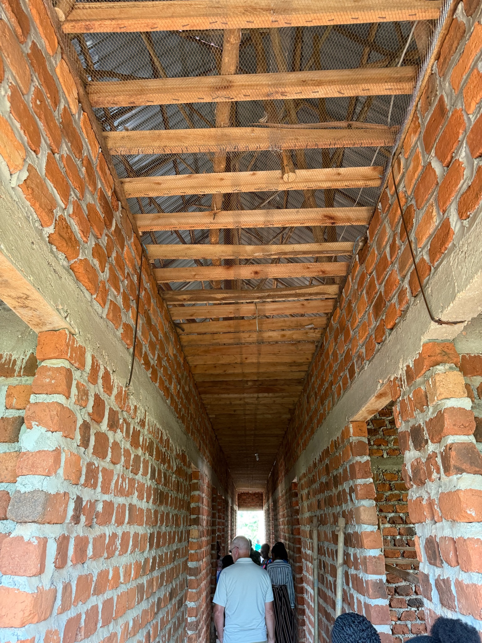 Visitors walking the unfinished brick hallway of the new girls' dormitory — timber rafters, no plaster yet.