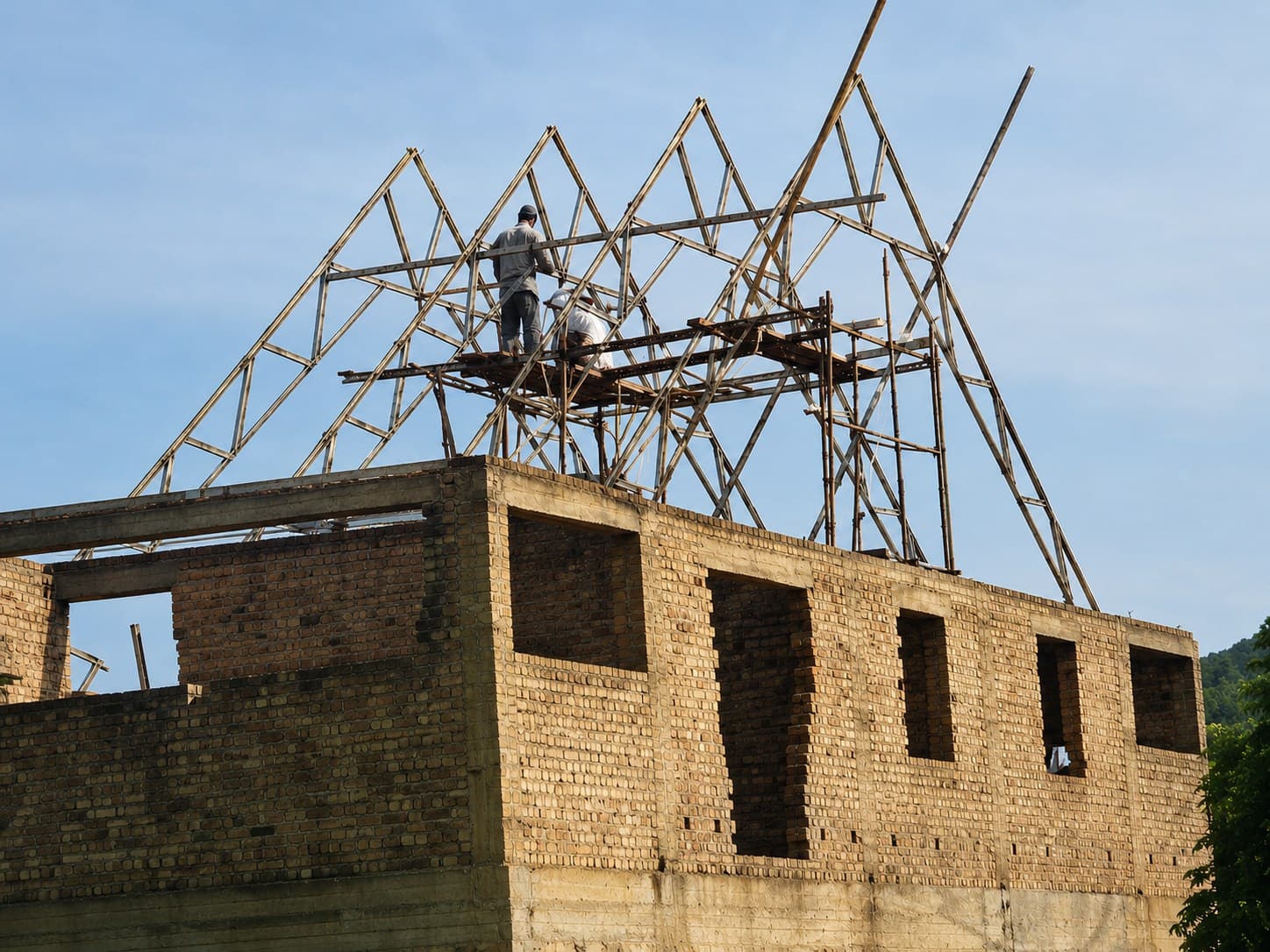 Bamboo roof trusses being raised over brick walls, 2012.